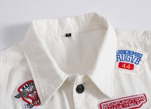 Close-up of white denim vest featuring colorful embroidery patches and metal button