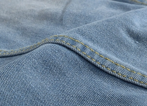 Macro detail of light blue denim fabric with reinforced yellow double stitching