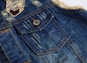 Macro detail of dark blue denim vest featuring vintage embroidery and frayed edges
