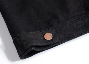 Detail shot of black denim vest with fine stitching and a bronze jeans metal button