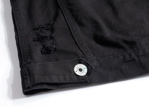 Détail macro du denim noir avec effet déchiré et bouton métallique gravé JEANS