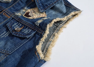 Detail of distressed dark blue denim vest with vintage patches and frayed armholes