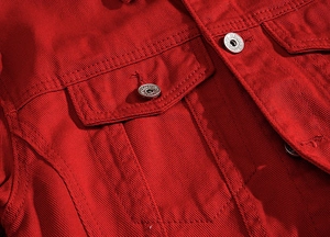 Close-up of red denim jacket featuring silver embossed metal buttons and flap pocket detail