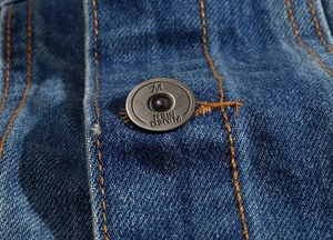 Macro shot of blue denim vest detail with orange stitching and vintage metal button