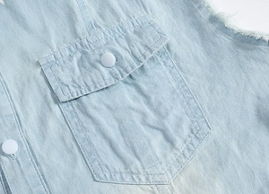 Close-up of light blue denim vest showing pocket detail with white button and frayed edges