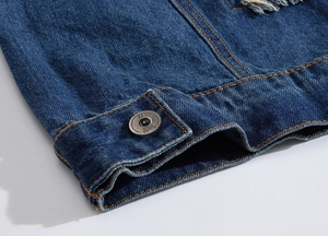 Detail of blue denim vest with metal button, orange stitching and distressed fabric texture