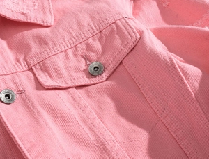 Dettaglio della giacca di jeans rosa che mostra la trama del tessuto e il bottone in metallo