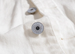 Nahaufnahme der gravierten Metallknöpfe auf einer weißen Jeansweste mit Textur