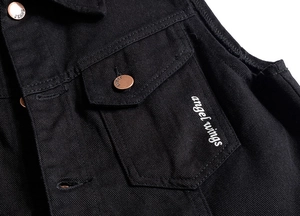 Detail of black denim vest showing copper button and angel wings embroidery on chest pocket