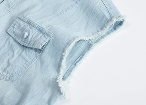 Close-up of light blue denim vest showing frayed sleeve edges and chest pocket detail