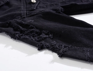 Dettaglio macro della giacca di jeans nera con strappi effetto vintage e bottone argento
