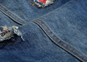Macro detail of men's denim vest featuring distressed holes and orange stitching