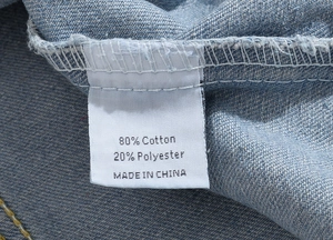 Macro view of product care label on light blue denim vest showing 80% cotton material