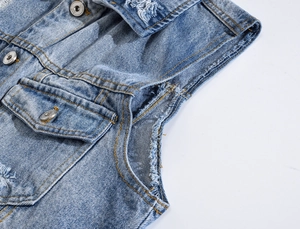 Detailed close-up of blue denim vest with distressed frayed edges and metal buttons