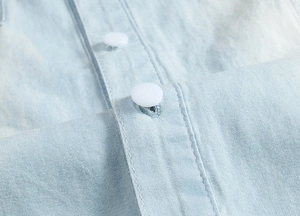 Close-up of light blue denim fabric texture with white buttons and fine stitching details
