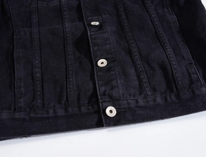 Dettaglio della giacca in denim nero con pieghe verticali e bottoni in metallo argentato