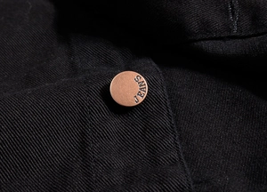 Macro view of a bronze metal button with JEANS engraving on black denim fabric vest