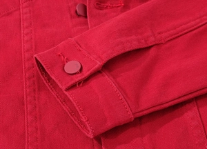 Detailed close-up of red denim jacket cuff with embossed metal button and stitching