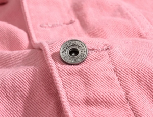 Macro shot of silver metal button and textured pink cotton denim fabric details