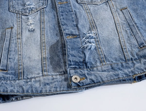 Macro detail of distressed light blue denim vest showing ripped texture and metal buttons