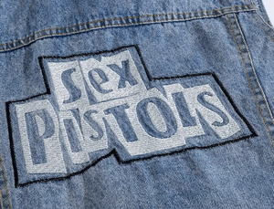 Detail of Sex Pistols white embroidered patch on light blue washed denim fabric