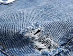 Close-up of distressed blue denim fabric with yellow stitching and ripped texture detail