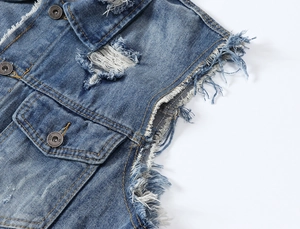Detailed macro view of distressed denim vest with frayed edges and metal buttons