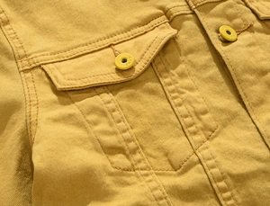 Detail of mustard yellow denim jacket showing flap chest pocket and metal jeans buttons