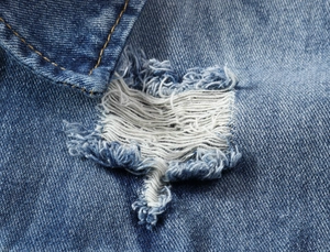 Detail view of distressed blue denim fabric with natural frayed holes and orange stitching