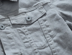 Detail of grey washed denim jacket featuring metal buttons and flap pocket stitching