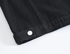 Dettaglio macro di gilet in denim nero con bottone in metallo argento e trama in twill