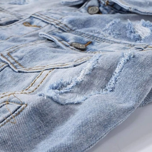 Detail of light blue denim vest showing distressed holes and silver metal buttons