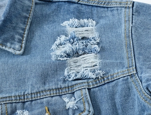 Detail van lichtblauw denim jack met zware slijtageplekken en oranje contraststiksels