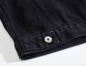 Dettaglio dell'orlo di una giacca in denim nero con bottone in metallo e trama diagonale