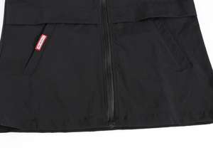 Close-up of black vest featuring resin zipper, slanted pockets, and red fashion label