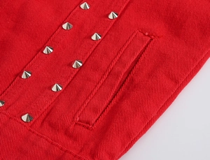 Detailed close-up of red denim fabric with silver metal cone studs and precision stitching