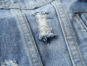 Detailed macro view of denim vest with frayed edges and orange contrast stitching