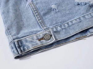 Detailed close-up of light blue denim vest with distressed edge and metal button