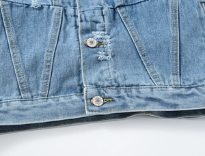 Detail van de distressed zoom op een lichtblauw spijkerjack met metalen knopen en gele stiksels