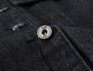 Détail macro d'un bouton en métal bronze gravé NEW DENIM sur un gilet en jean gris foncé