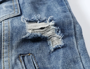Detail of distressed blue denim fabric with ripped hole design and yellow contrast stitching