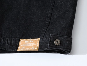 Détail de l'ourlet du gilet en denim noir avec étiquette en cuir et bouton métal