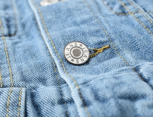 Detail van lichtblauwe denim met reliëf metalen jeansknoop en gele contrasterende stiksels