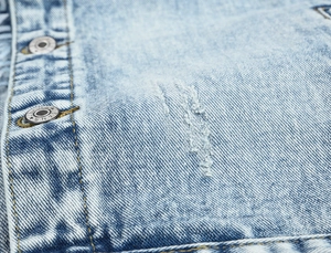 Detailed macro view of light blue washed denim fabric with distressed texture and metal buttons