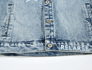 Detail of light blue washed denim jacket featuring metal star buttons and RELARSE print