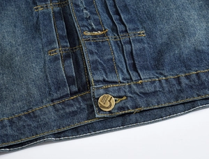 Détail macro du denim bleu délavé avec bouton en métal vintage et surpiqûres jaunes