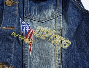 Close-up of men's denim vest featuring lightning embroidery and washed fabric detail