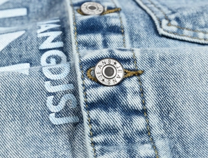 Detail of light blue denim fabric featuring silver metal buttons with JEANS engraving