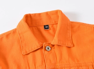 Detail der leuchtend orangefarbenen Jeansjacke mit Metallknöpfen und Köperstruktur