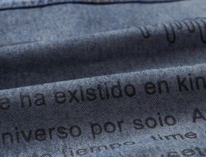 Detail of blue denim vest featuring black letter print and distressed fabric texture